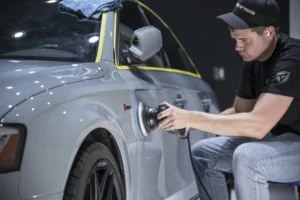 A man is performing auto detailing training on a car in a showroom.