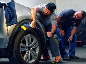 Two men inspecting and repairing a car tire with tools during a PDR training workshop.