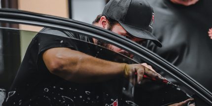 A man wearing a cap specializes in window tinting, concentrating intently on his task.