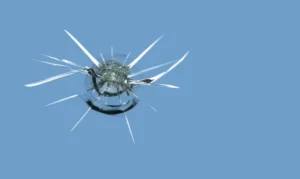 Close-up of a cracked windshield with a radial, web-like pattern on a clear blue background.