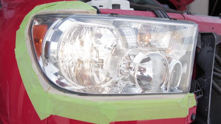 A car's headlight covered with green masking tape, likely for protection during a headlight renewal repair.