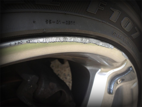 Close-up of car tire sidewall damage showing visible scuff marks and abrasions against a blurry background, highlighting the need for wheel repair.